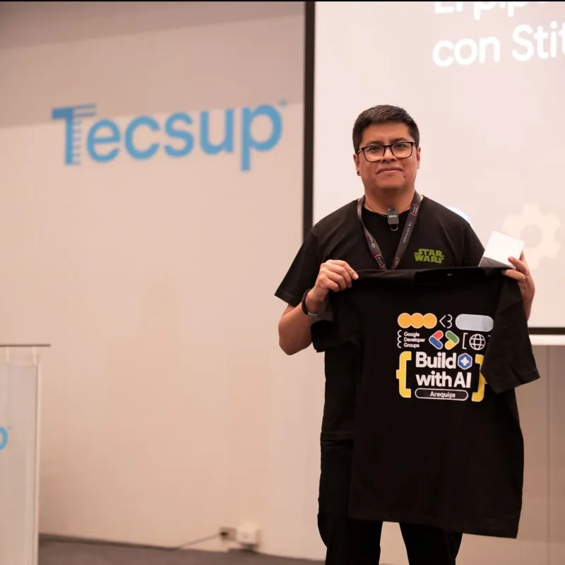 Vik Castro holding a Build with AI Arequipa t-shirt at a GDG Arequipa session at Tecsup